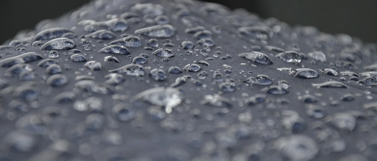 Щільне поле водяних крапель на сірій поверхні: дрібні злилися в більші, по краях кадр іде в розмиття